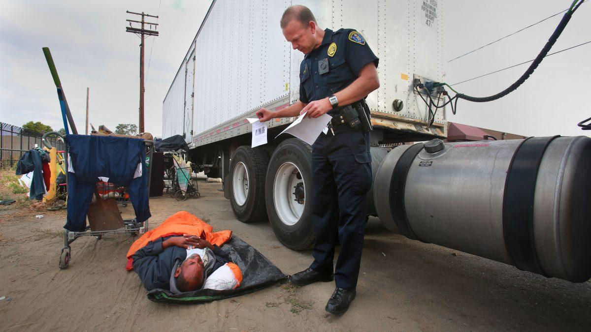 A homeless man rolls over to look at a flyer with pictures of a suspect in recent assaults on the homeless, as a San Diego Homeless Outreach Team officer canvasses several areas in San Diego on July 6, 2016. (Peggy Peattie/U-T San Diego)