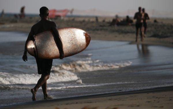 A surfer carries his surfboard at a beach in Malibu, Calif., on Aug. 21, 2018. (Mario Tama/Getty Images)