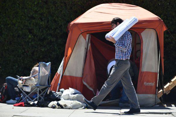 A man carrying blueprints passes a homeless encampment in San Francisco, California on June, 27, 2016. (Josh Edelson/AFP/Getty Images)