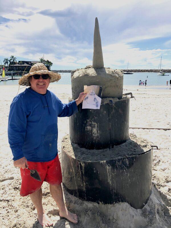 Sand sculptor Chris Crosson stands with the preliminary structure he'll form into a sandy narwal in Dana Point, Calif., on March 7, 2020. (Chris Karr/The Epoch Times)