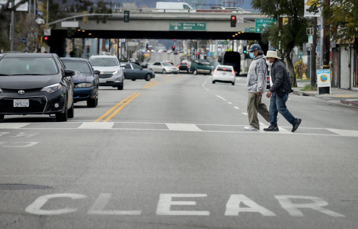 Men cross a street wearing face masks amid the COVID-19 pandemic in Los Angeles, California on April 6, 2020. (Mario Tama/Getty Images)