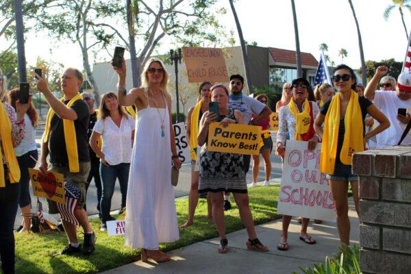 Parents hold signs and cellphones at a gathering to protest mandated school closures due to the COVID-19 pandemic in Santa Ana, Calif., on Aug. 4, 2020. (Jamie Joseph/The Epoch Times)