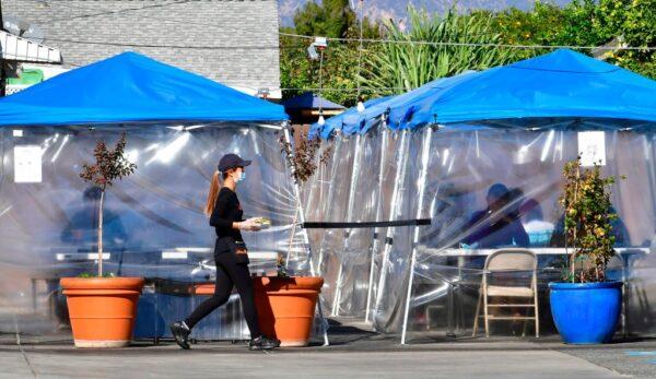 A waitress delivers orders to diners seated outdoors under tents in a restaurant's parking lot in Alhambra, Calif., on Nov. 17, 2020. (Frederic J. Brown/AFP via Getty Images)