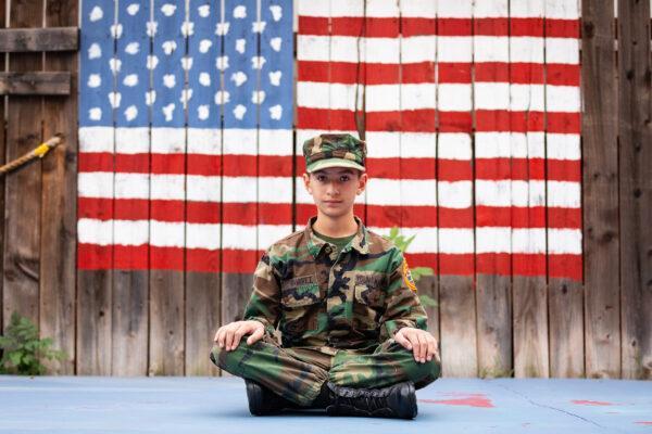 Jordan Ramirez, 11, sits in front of an American flag painted on the fence at his home in La Puente, Calif., on Jan. 19, 2021. (John Fredricks/The Epoch Times)