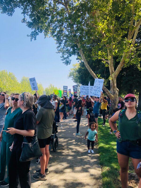 Protesters with flags, banners, and signs stand along the sidewalk in Roseville, Calif., on Aug. 9, 2021. (Courtesy of Denise Aguilar)