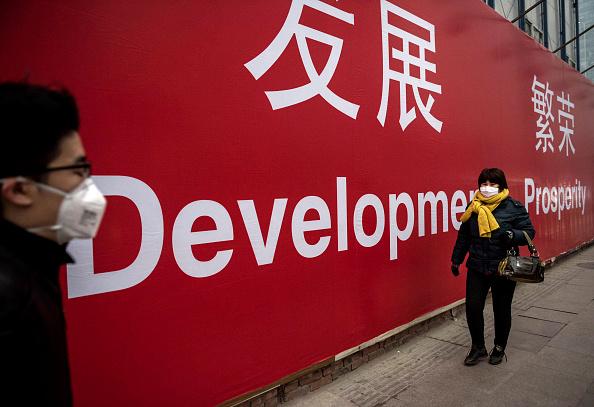 Chinese citizens wear face masks as they walk past a billboard reading "Development" and "Prosperity" during heavy smog in Beijing on Nov. 29, 2014. (Kevin Frayer/Getty Images)