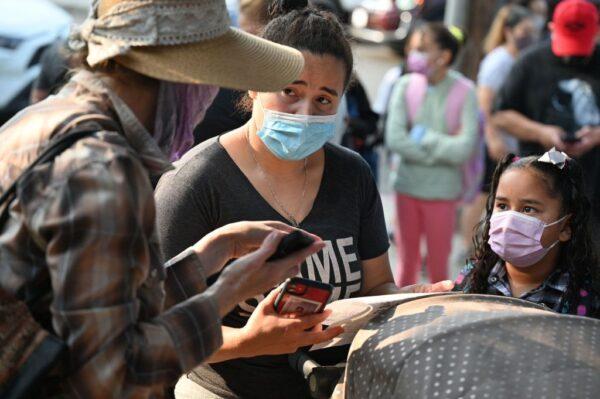 A volunteer (L) helps a parent understand how to access the Daily Pass health screening data on her cellphone, on the first day of the school year at Grant Elementary School in Los Angeles, Calif., August 16, 2021.
