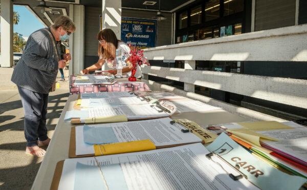 Huntington Beach resident Cari Swan helps a woman fill out her information to place her signature to recall Huntington Beach Mayor Kim Carr and city councilmembers in front of a grocery store. Volunteers extended their time by one hour on Feb. 6, 2022. (John Fredricks/The Epoch Times)