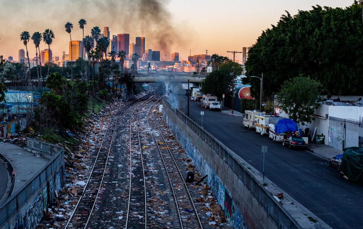 Smoke from a fire at a homeless encampment is seen near railroad tracks littered with boxes left behind from stolen items in Los Angeles on Jan. 2, 2022. (John Fredricks/The Epoch Times)