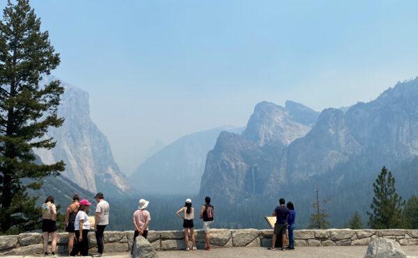 Visitors check out the view from the east end of the Wawona Tunnel into Yosemite Valley, showing three major landmarks, from the left, El Capitan, Half Dome, and Bridalveil Fall, obscured by thick smoke in the area from the wildfire burning to the south in the Mariposa Grove of Giant Sequoias, at Yosemite National Park, Calif., on July 9, 2022. (Courtesy of U.S. National Park Service/Handout via Reuters)