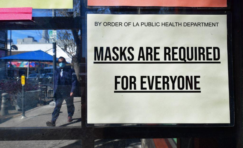 A man wearing a protective face mask walks past a sign requiring face masks posted on a storefront in Los Angeles on March 2, 2022. (Frederic J. Brown/AFP via Getty Images)