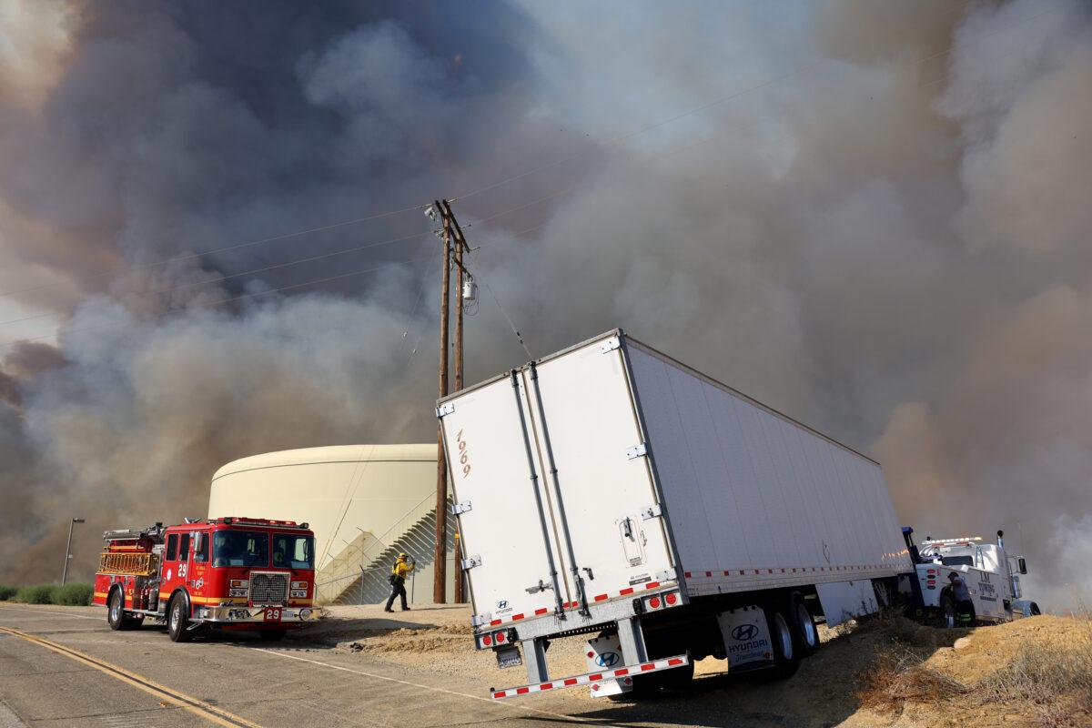 Firefighters work as a tow truck prepares to tow away the trailer of a truck while the Route Fire burns nearby, near Castaic, California, on Aug. 31, 2022. (Mario Tama/Getty Images)