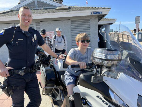Newport Beach Police Department Officer Mark Hamilton shares his motorcycle with a young Mobile Cafe attendee in Newport Beach on Feb. 4, 2023. (Courtesy of Newport Beach Police Department)