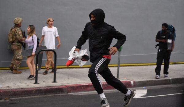 A suspected looter carrying boxes of shoes run past National Guard soldiers in Hollywood, Calif., on June 1, 2020, after a demonstration over the death of George Floyd. (Robyn Beck/AFP via Getty Images)