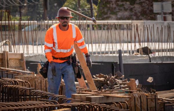 A worker tosses a hammer to a colleague as construction continues on the Highway 73 southern interchange from the 405 freeway in Costa Mesa, Calif., on April 21, 2022. (John Fredricks/The Epoch Times)