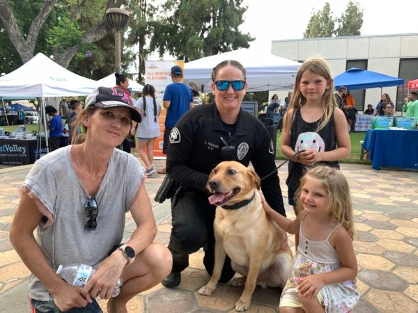 Jennifer Burkhalter (L) and her two daughters pose with a police officer and her K9 partner at a National Night Out event at Pomona Civic Center in Pomona, Calif., on Aug. 1, 2023. (Linda Jiang/The Epoch Times)
