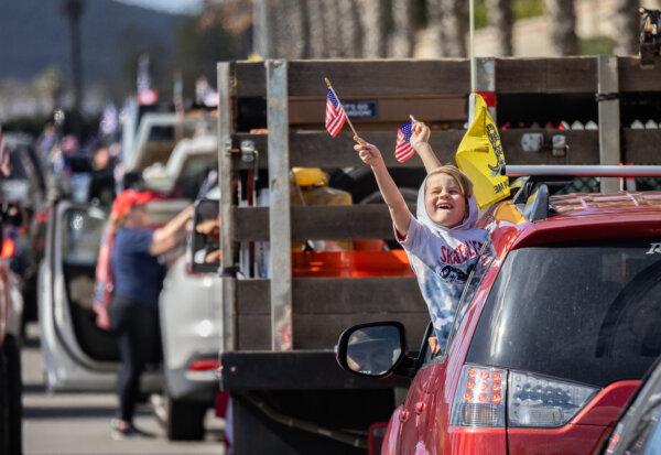 Children wave U.S. flags outside a car window in San Ysidro, Calif., on Feb. 3, 2024. (John Fredricks/The Epoch Times)