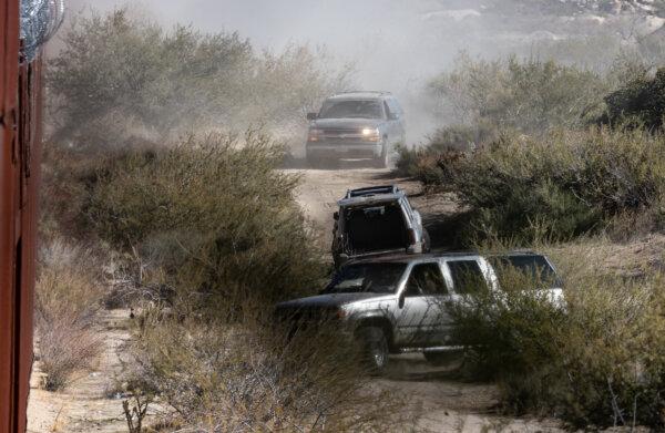 Mexican cartel members drive SUV's containing dozens of migrants race to an open gap in the United States border wall near Jacumba, Calif., on Dec. 6, 2023. (John Fredricks/The Epoch Times)