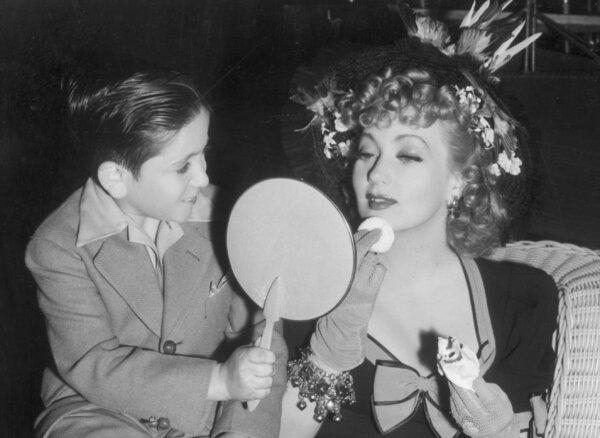 A young actor holds up a mirror while American actor Ann Sothern (born Harriette Lake), uses a powder puff on her chin on the set of the film "Maisie Was a Lady" in 1941. (Hulton Archive/Getty Images)