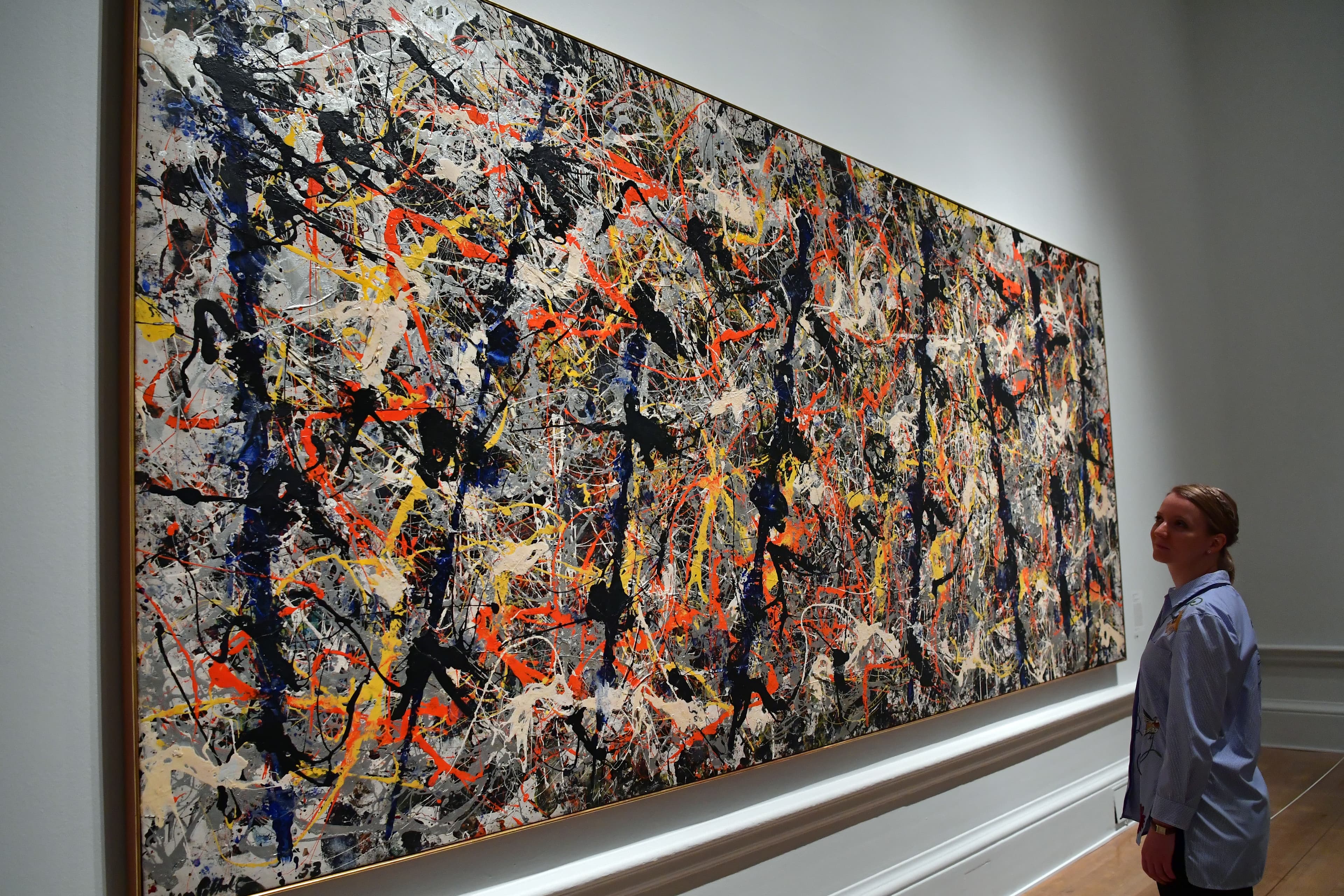 A member of staff poses next to a painting by U.S artist Jackson Pollock entitled "Blue Poles" at the Royal Academy of Arts in London on Sept. 20, 2016. (Carl Court/Getty Images)