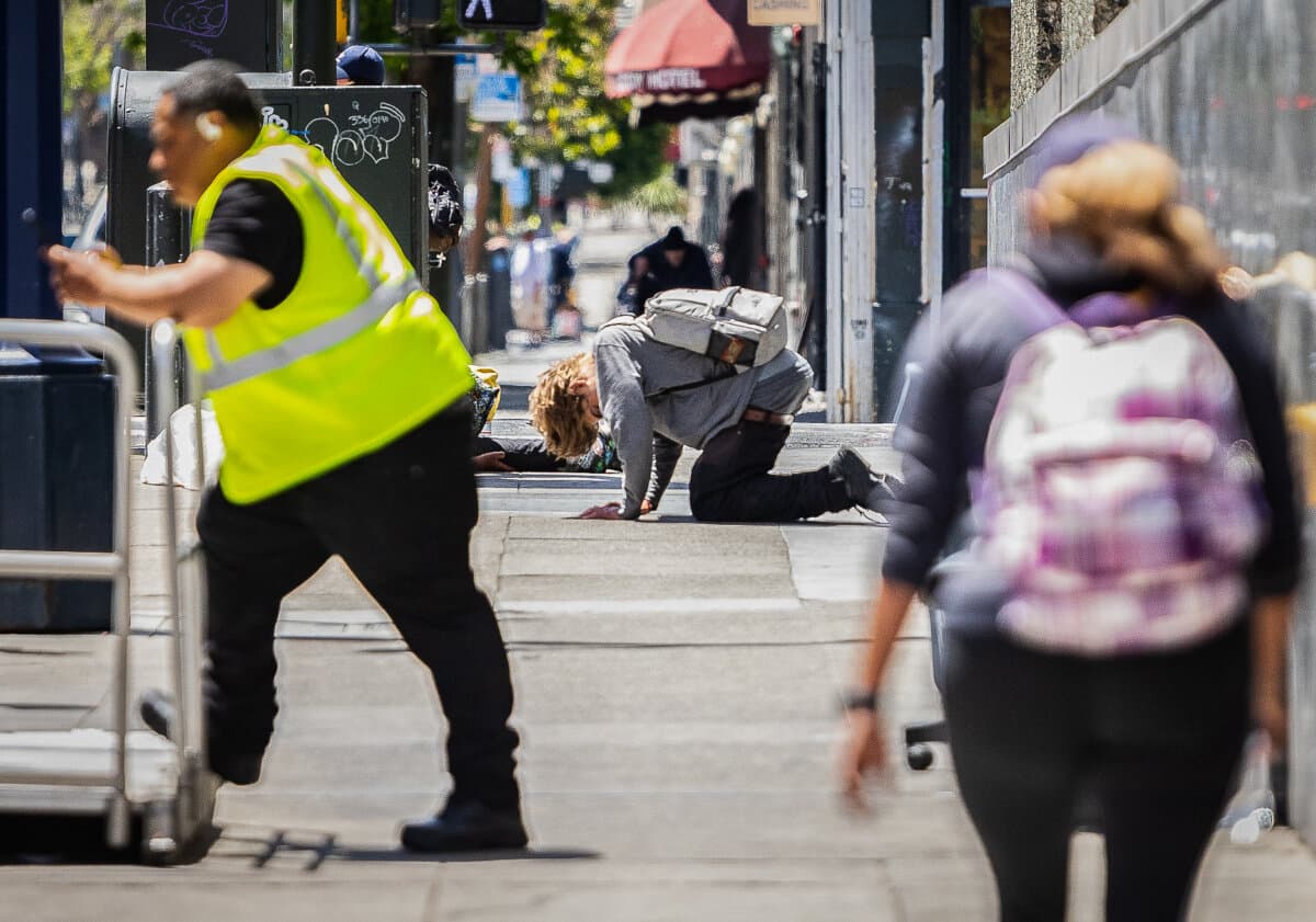 People walk around a person under the influence of drugs in the Tenderloin District of San Francisco on May 16, 2024. (John Fredricks/The Epoch Times)