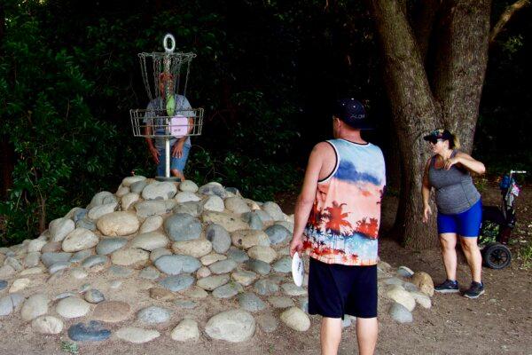 Players finish their putts on the sixth hole of league play at the disc golf course in Reichmuth Park in Sacramento, Calif., on May 30, 2024. (Travis Gillmore/The Epoch Times)