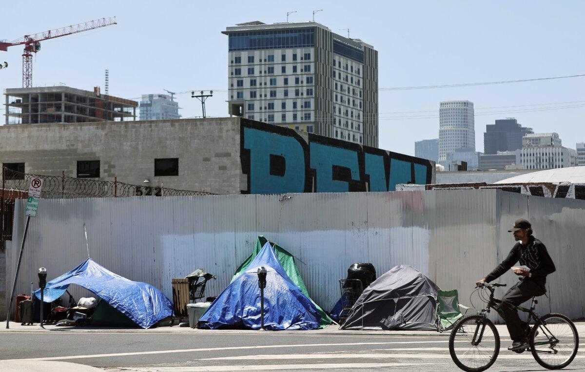 A cyclist passes an encampment of homeless people in the Skid Row community in Los Angeles on June 28, 2024. (Mario Tama/Getty Images)