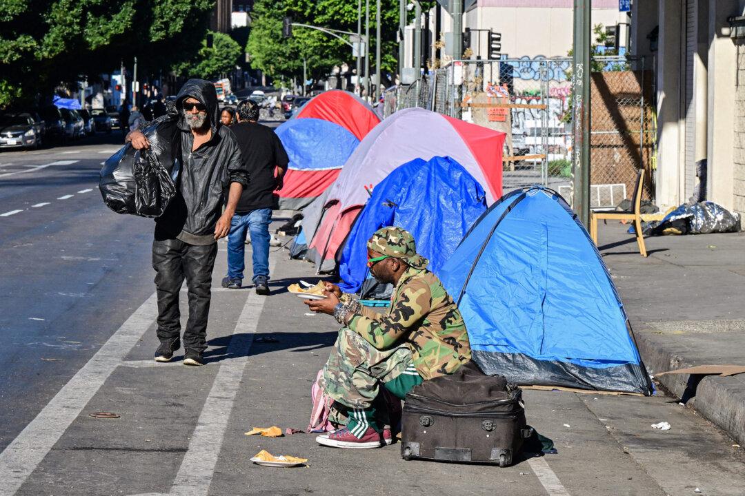 A homeless man sits on a suitcase on a street lined with tents in downtown Los Angeles on Nov. 22, 2023. (Frederic J. Brown/AFP via Getty Images)