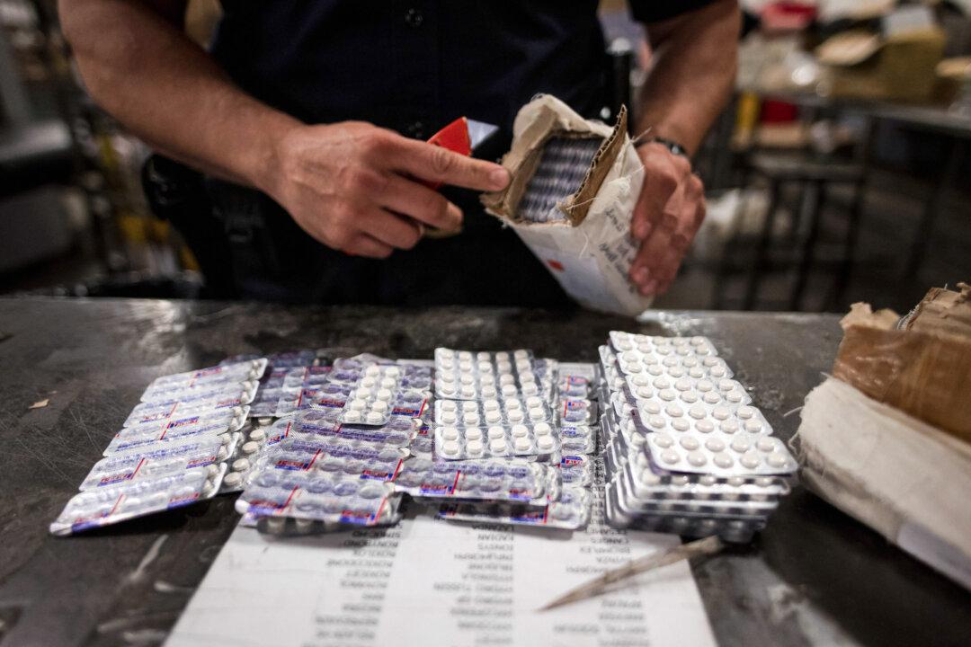 (Top) People stand in line to be checked by U.S. Customs and Border Protection agents at the San Ysidro Port of Entry in California, on Oct. 2, 2019. (Bottom Left) An officer from the U.S. Customs and Border Protection, Trade, and Cargo Division finds oxycodone pills in a parcel at John F. Kennedy International Airport’s U.S. Postal Service facility in New York on June 24, 2019. (Bottom Right) A U.S. Customs and Border Protection agent weighs a package of fentanyl at the San Ysidro Port of Entry in California, on Oct. 2, 2019. (Sandy Huffaker/AFP via Getty Images, Johannes Eisele/AFP via Getty Images).