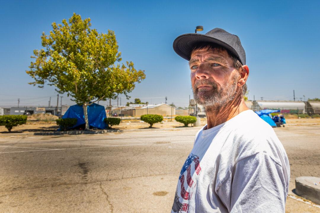 Michael, a homeless man, passes by an area with tents housing the homeless, near Lancaster, Calif., on July 10, 2024. (John Fredricks/The Epoch Times)