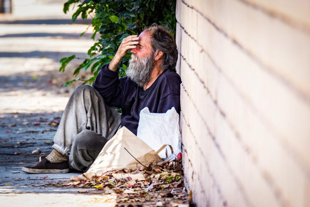 (Top) A homeless man walks with his belongings along a street in Santa Ana, Calif., on July 15, 2024. (Bottom) A homeless individual rests by a busy street in Santa Ana, Calif., on July 15, 2024. (John Fredricks/The Epoch Times)