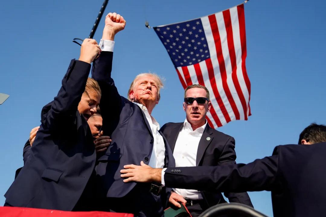 A video (top) and a photo (bottom) show former President Donald Trump raising his fist while being escorted off the stage at the rally. (Bottom) Former President Donald Trump is surrounded by U.S. Secret Service agents at a campaign rally, in Butler, Pa., on July 13, 2024. (NTD, Evan Vucci/AP Photo)