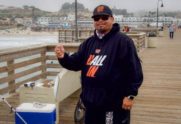 John Ramos holds a mackerel that he caught while fishing from the Pismo Beach pier in Southern California on July 18, 2024. (Travis Gillmore/The Epoch Times)