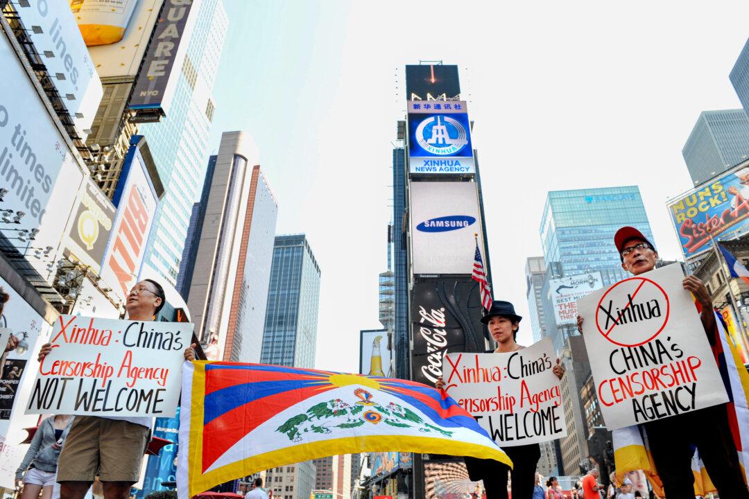 People hold signs to protest an electronic billboard (top) leased by Xinhua, a state-run news agency operated by the Chinese regime, as it makes its debut in New York's Times Square on Aug. 1, 2011. (Stan Honda/AFP via Getty Images)