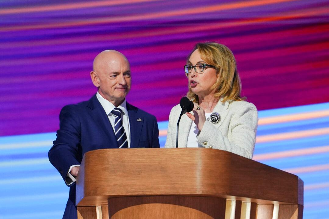 Sen. Mark Kelly (D-Ariz.) looks on as former Representative from Arizona Gabby Giffords speaks during the last day of the Democratic National Convention in Chicago on Aug. 22, 2024. (Madalina Vasiliu/The Epoch Times)