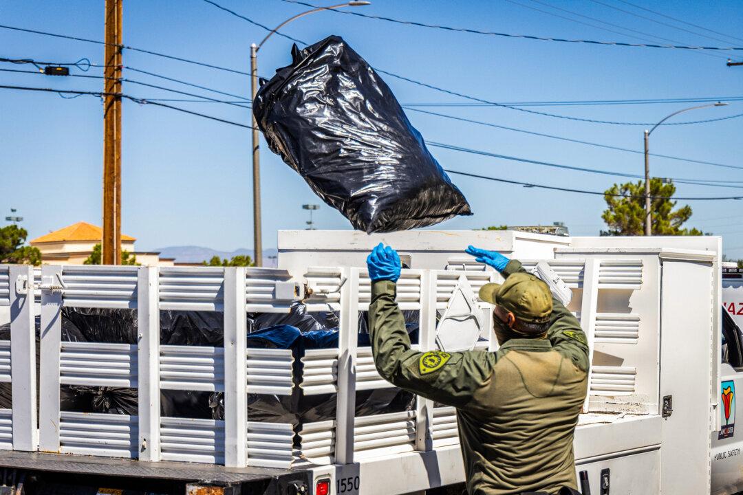 A police officer (L) tosses a bag (R) of confiscated marijuana into the back of a truck. (John Fredricks/The Epoch Times)