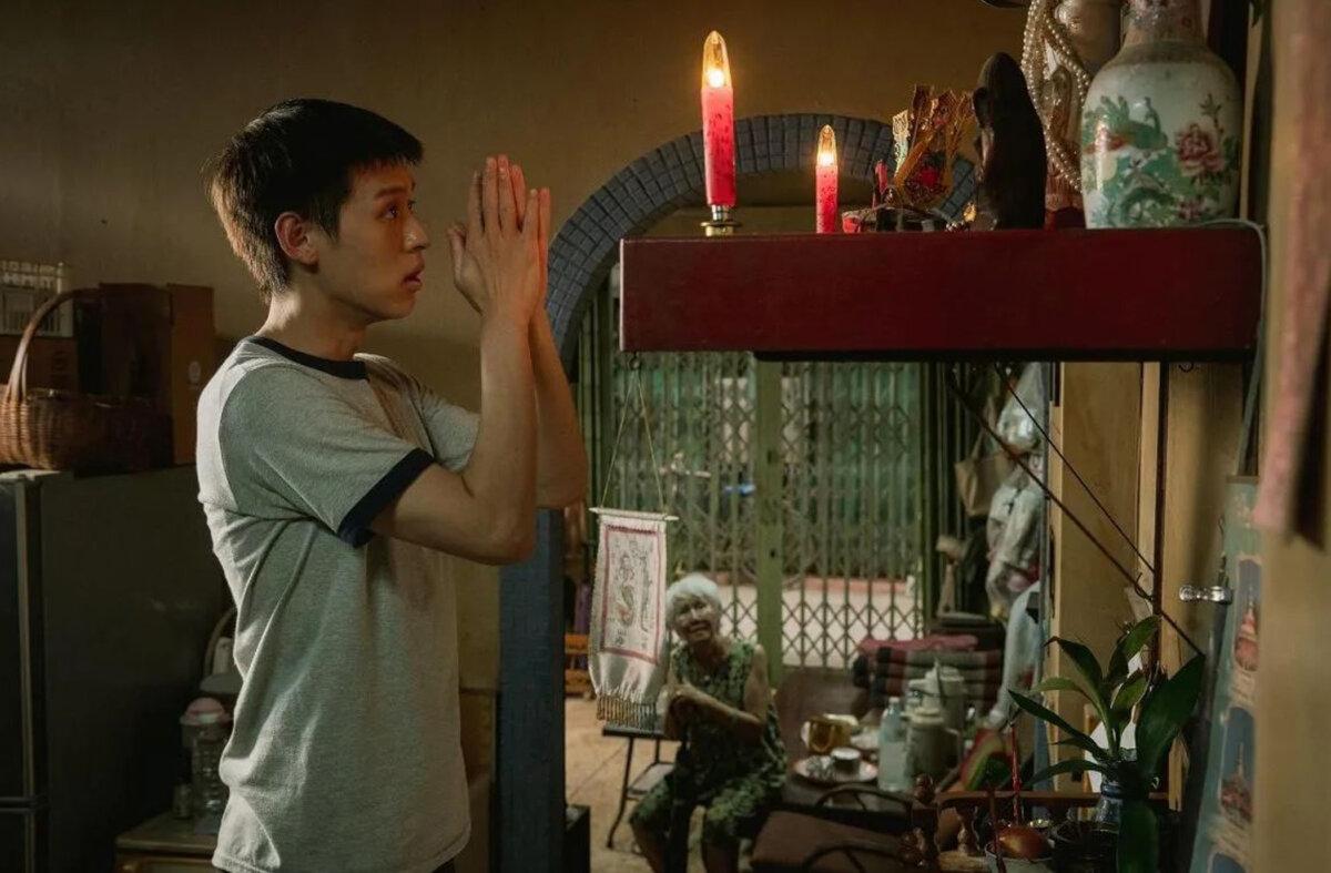 M (Putthipong Assaratanakul) prays as Amah (Usha Seamkhum) looks on, in “How to Make Millions Before Grandma Dies.” (GDH)