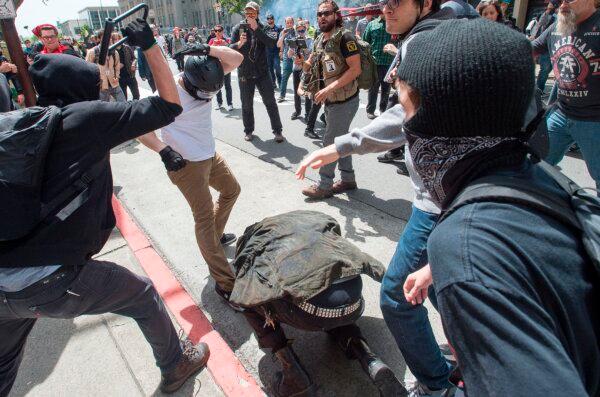 A man crouching for cover (C) gets hit with a bike lock as multiple fights break out between Trump supporters and anti-Trump protesters in Berkeley, Calif., on April 15, 2017. Hundreds of people with opposing opinions on then President Donald Trump threw stones, lit fires, tossed explosives and tear gas and attacked each other with makeshift weapons. (Josh Edelson/AFP via Getty Images)