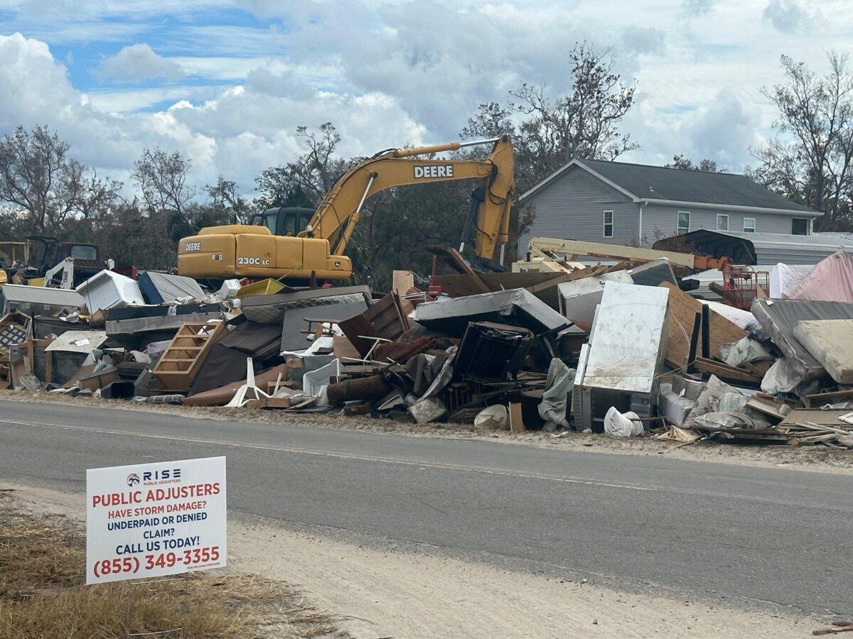 An equipment operator uses an excavator to move debris from a home destroyed by Hurricane Helene to the street for removal in Steinhatchee, Fla., on Oct. 5, 2024. (Nanette Holt/The Epoch Times)