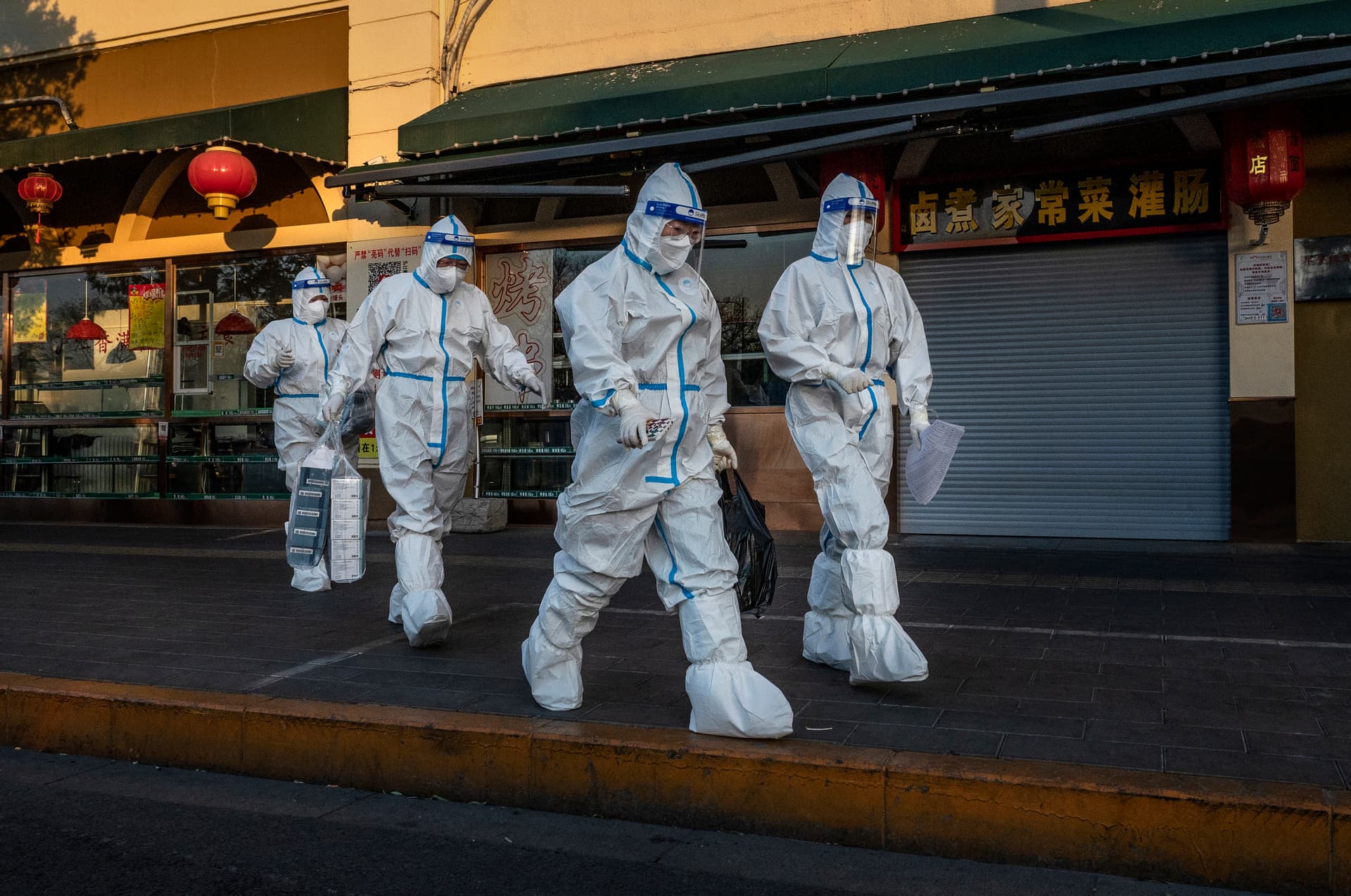 Pandemic control workers walk by a closed shop near a community with residents under health monitoring for COVID-19 in Beijing on Dec. 4, 2022. (Kevin Frayer/Getty Images)