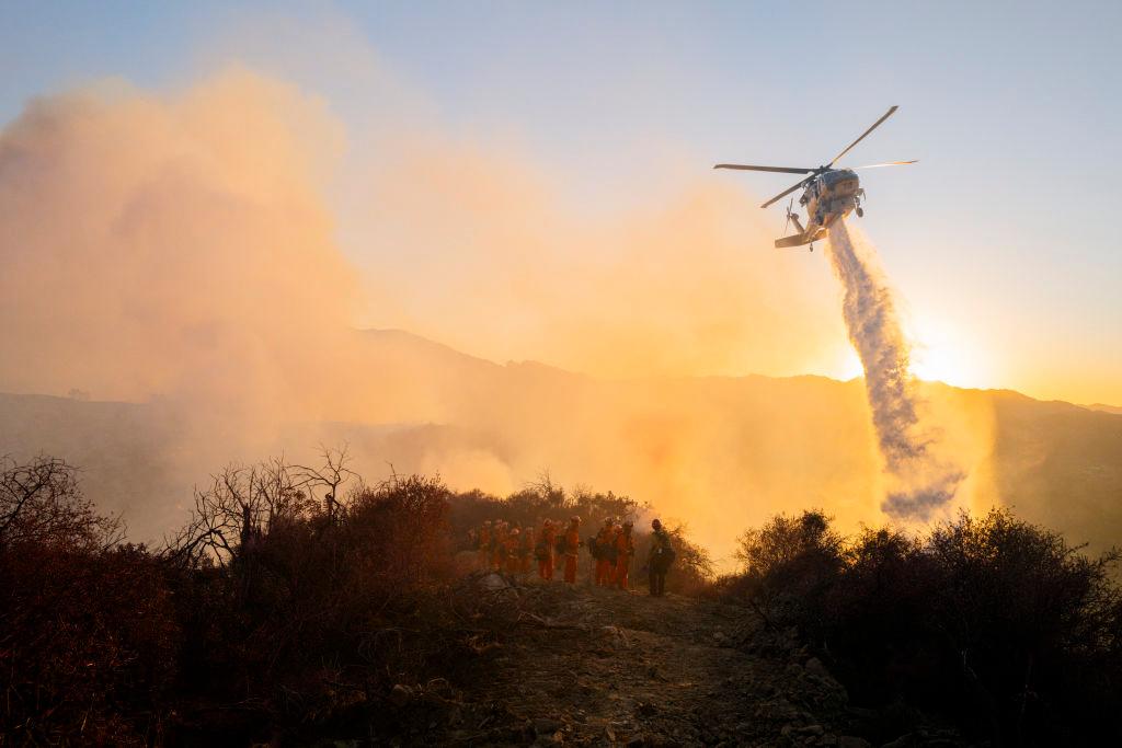A firefighting helicopter drops water while smoke rises from the growing Palisades fire in Los Angeles on Jan. 11, 2025. (Ali Matin/Middle East Images/AFP via Getty Images)