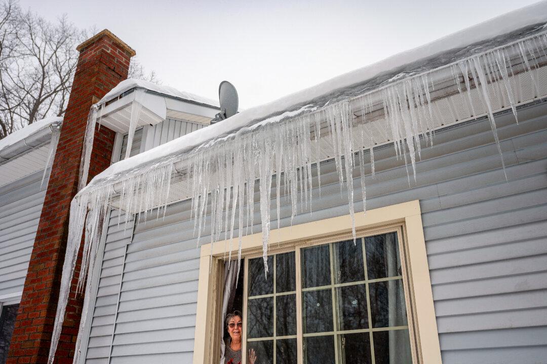 Claire Gagne peeks out from underneath an impressive curtain of icicles on her home in Lewiston, Maine, on Feb. 13, 2025. (Andree Kehn/Sun Journal via AP)