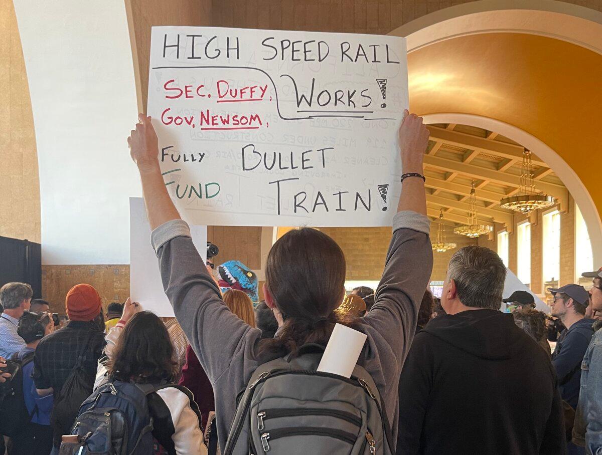 Protesters hold signs during the press conference at Union Station on Feb. 20, 2025. (Beige Luciano-Adams/The Epoch Times)