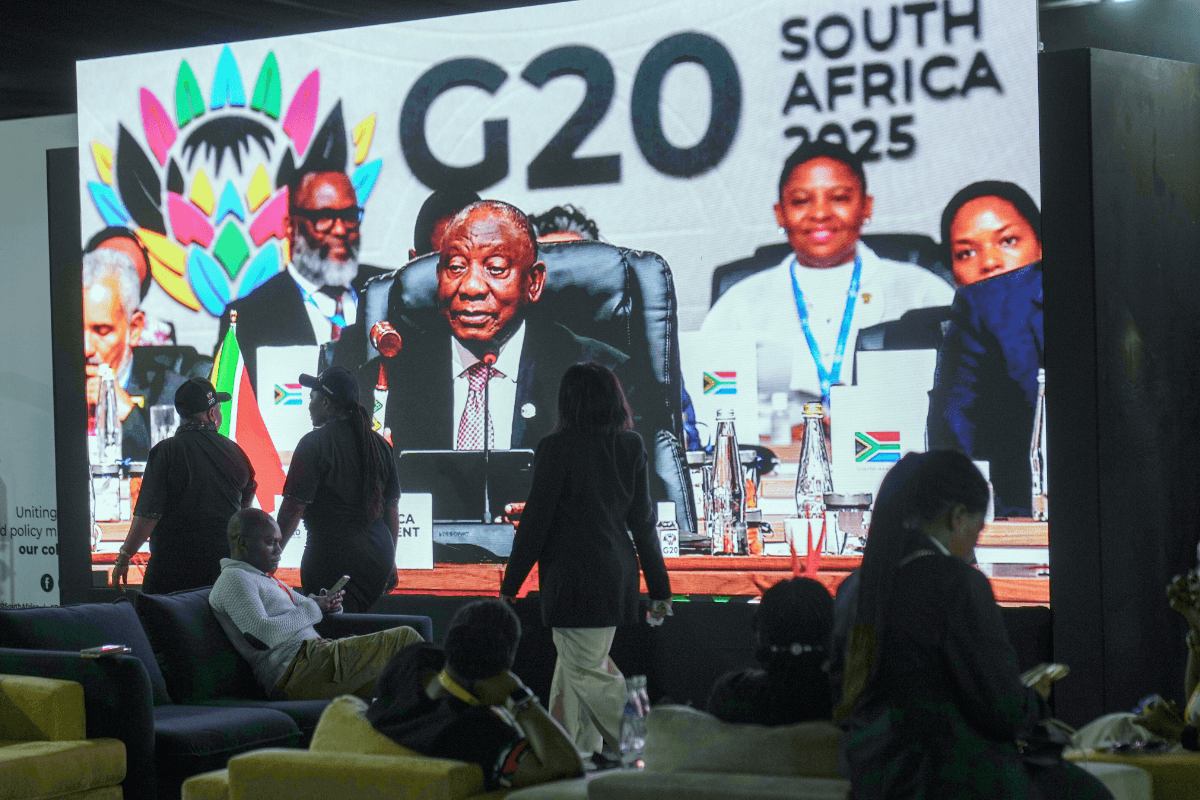 People walk by a large screen showing South African President Cyril Ramaphosa holding a wooden gavel as he officially closes the G20 leaders' summit, in Johannesburg on Nov. 23, 2025. (Jerome Delay/AP Photo)