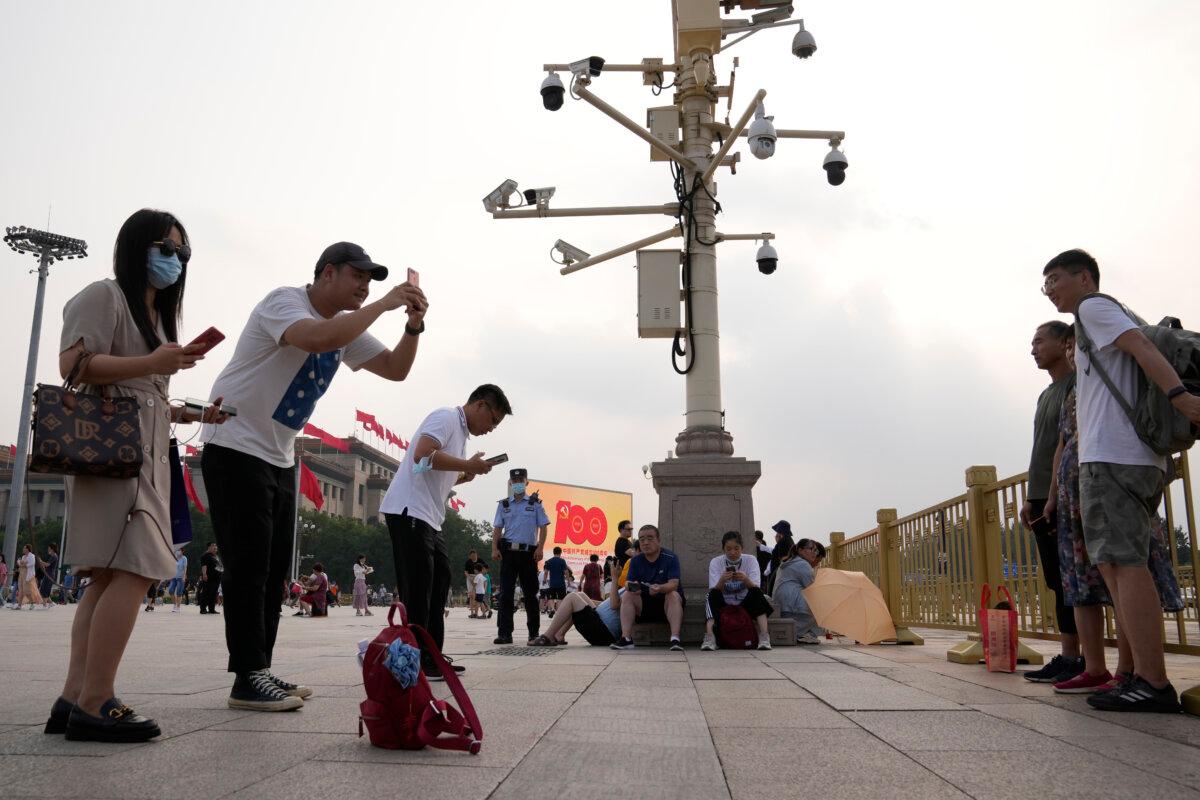 A policeman stands watch next to surveillance cameras as people take photos on Tiananmen Square in Beijing on July 15, 2021. (Ng Han Guan/AP Photo)