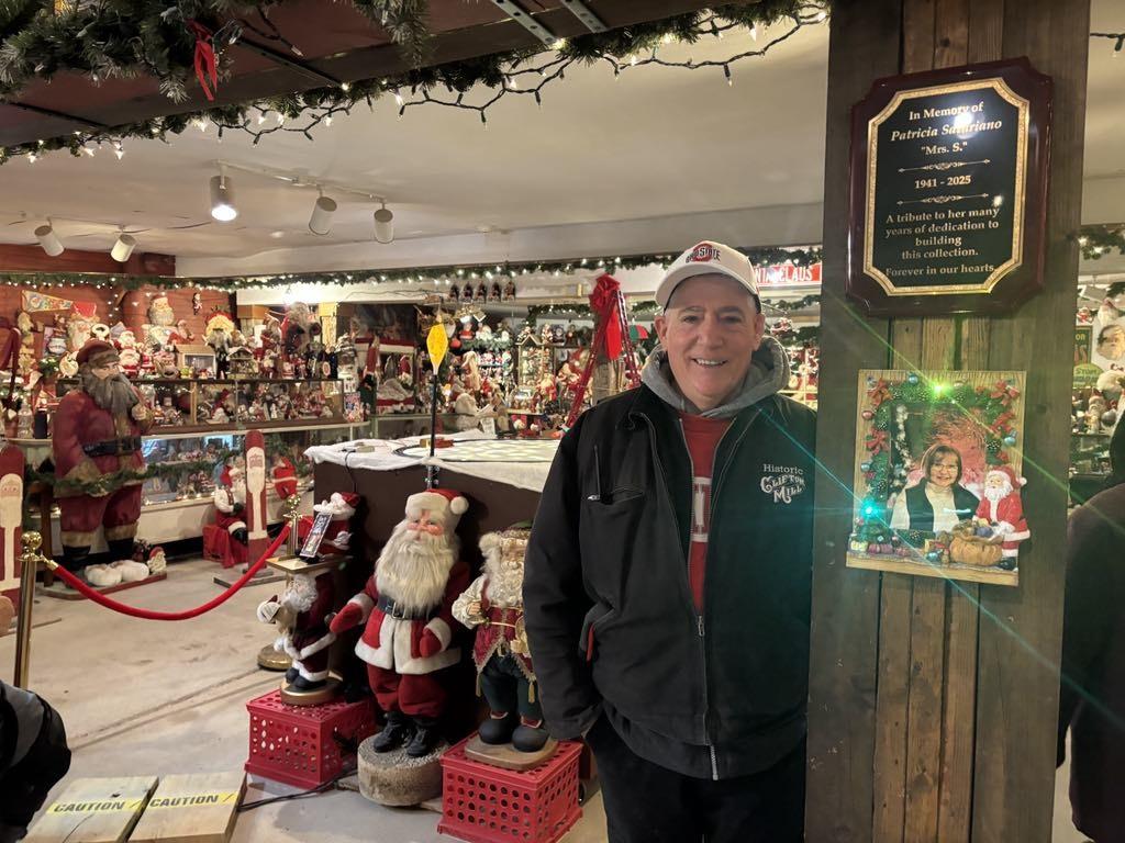 Anthony Satariano Jr. stands next to a photo of his mother, Patricia Satariano, at Clifton Mill's Santa Claus museum in Ohio on Dec. 8, 2025. (Jeff Louderback/The Epoch Times)