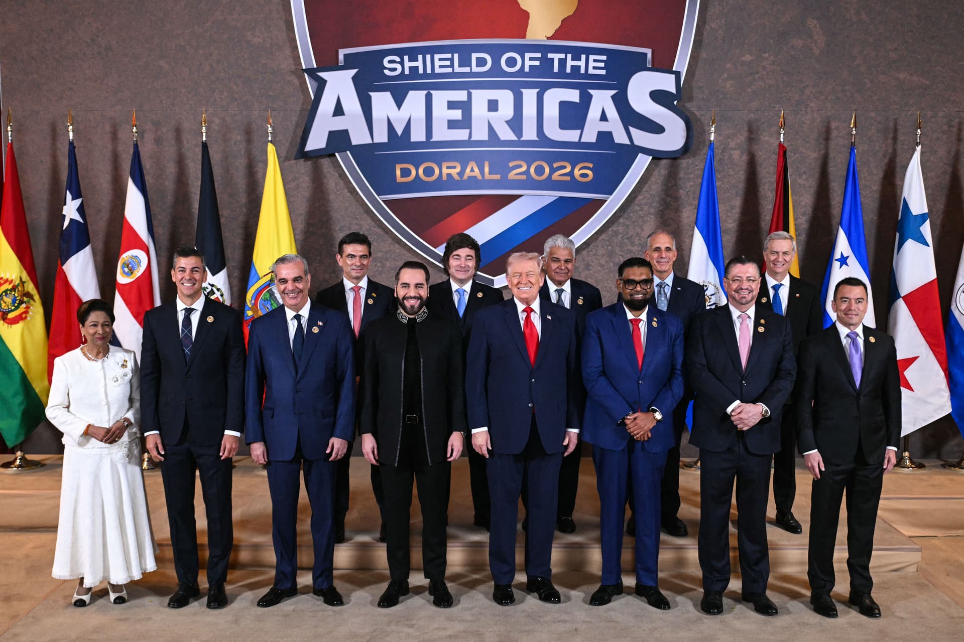 U.S. President Donald Trump (C) stands with, (L-R), Trinidad and Tobago's Prime Minister Kamla Persad-Bissessar, President of the Republic of Paraguay Santiago Peña, President of the Dominican Republic Luis Abinader, President of Bolivia Rodrigo Paz Pereira, President of El Salvador Nayib Bukele, President of Argentina Javier Milei, President of Panama José Raúl Mulino, President of Guyana Mohamed Irfaan Ali, President of Honduras Nasry "Tito" Asfura, President of Costa Rica Rodrigo Chaves Robles, President-elect of Chile José Antonio Kast, and President of Ecuador Daniel Roy Gilchrist Noboa Azín during a group photograph at the start of the "Shield of the Americas" Summit at Trump National Doral in Miami on March 7, 2026. (Saul Loeb/AFP via Getty Images)