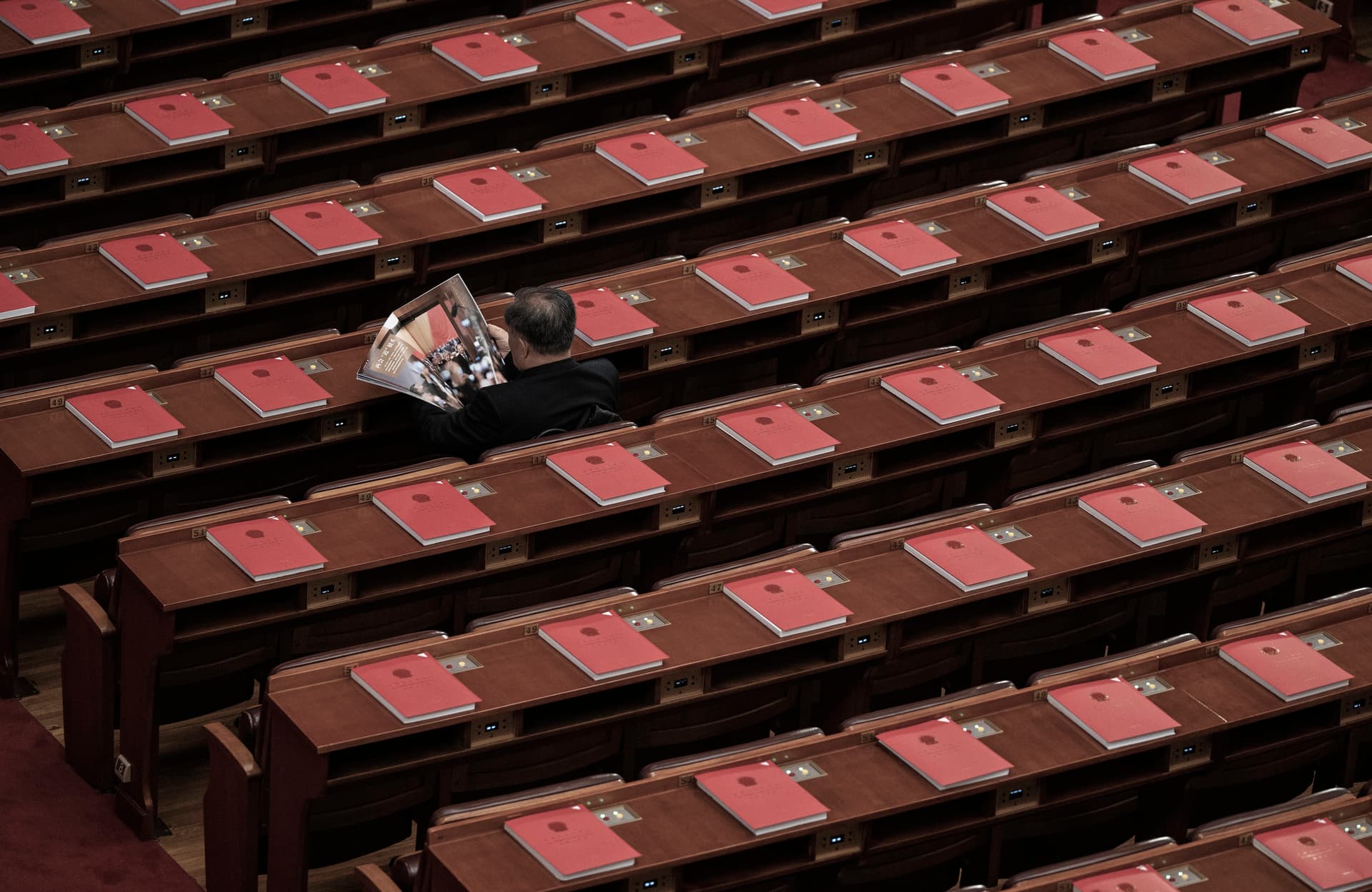 Red books on the desks as a delegate reads a magazine about the meetings before the closing session of the National People's Congress at the Great Hall of the People in Beijing on March 12, 2026. (Kevin Frayer/Getty Images)