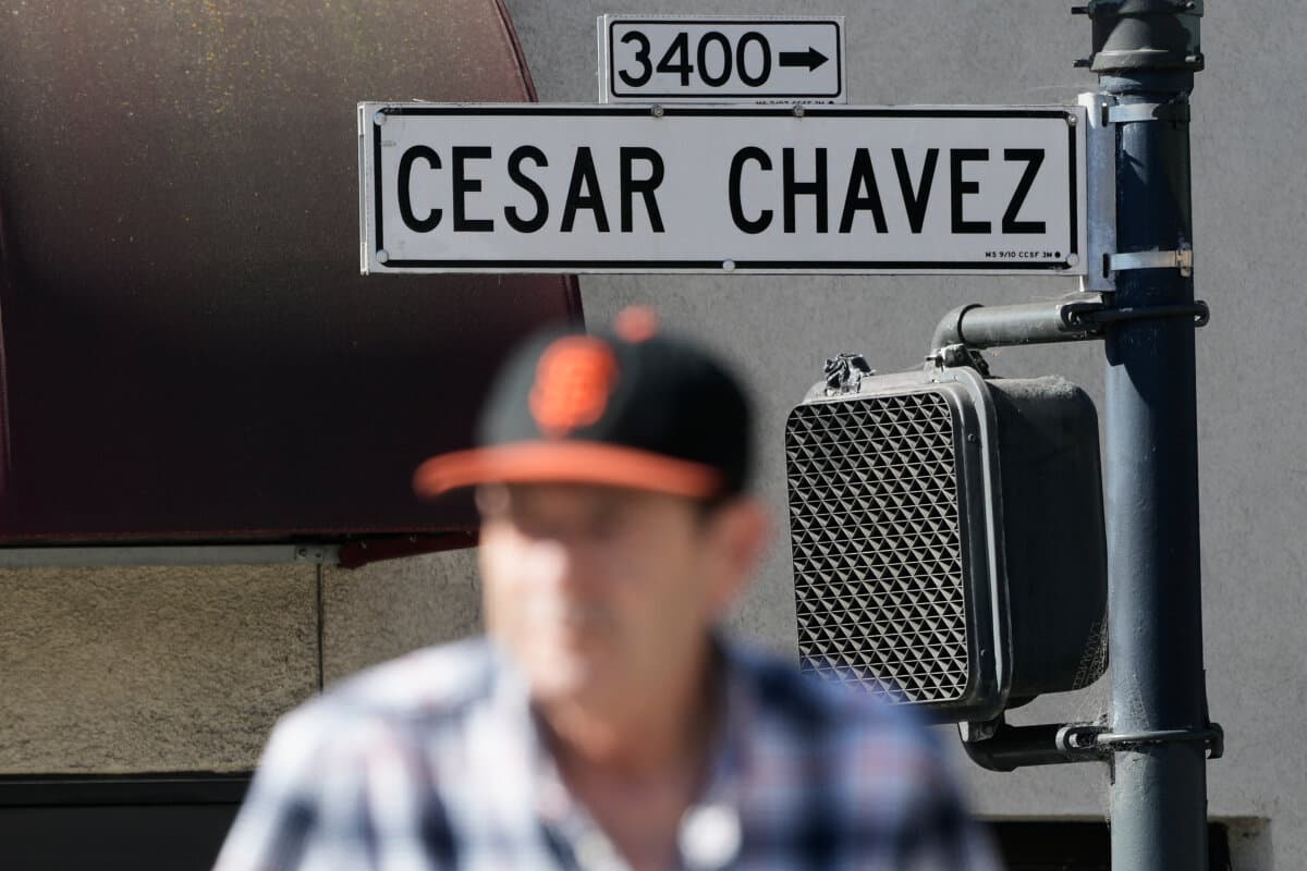 A pedestrian walks below a Cesar Chavez Street sign in San Francisco, Wednesday, March 18, 2026. (AP Photo/Jeff Chiu)