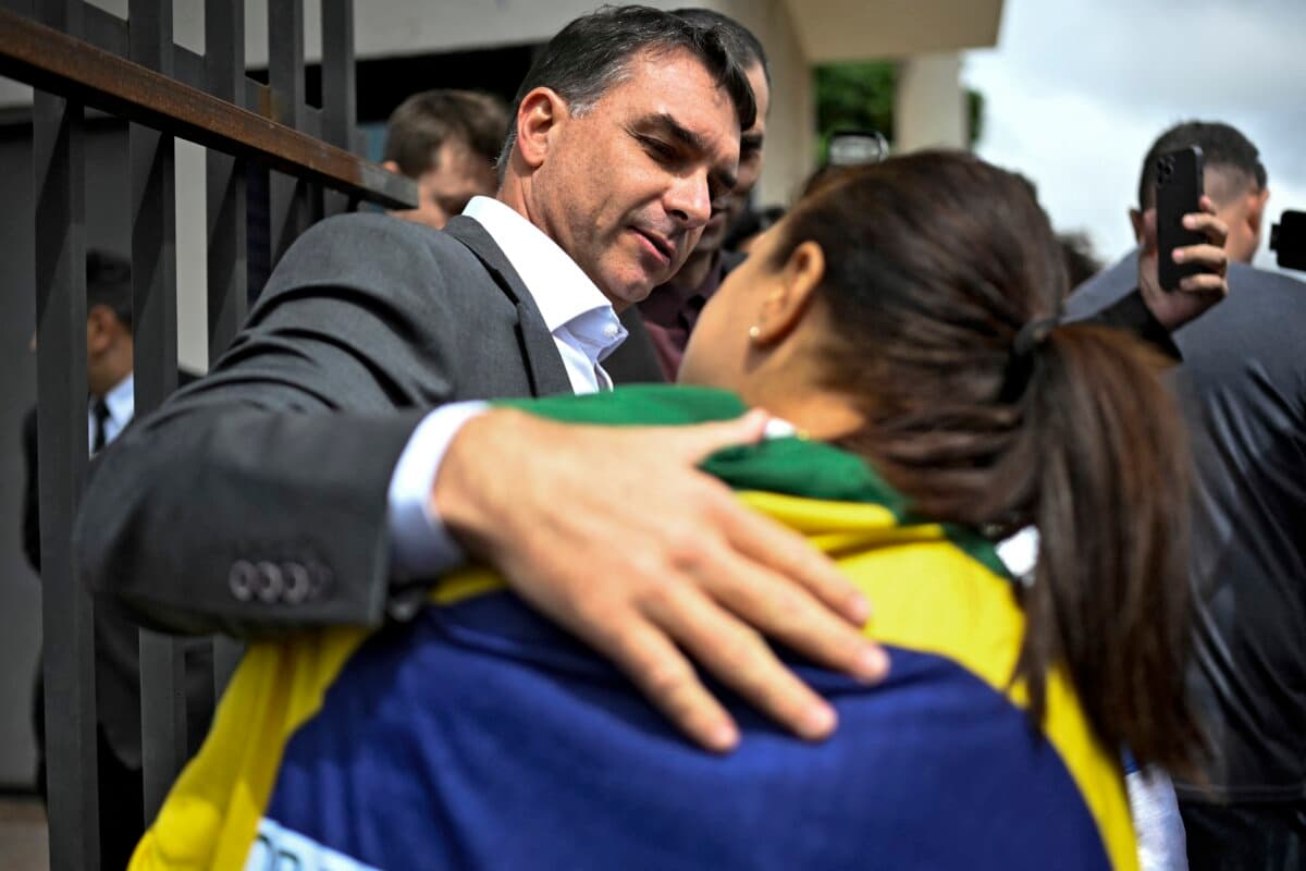 Senator Flavio Bolsonaro, son of former Brazilian President Jair Bolsonaro, greets a supporter as he leaves the Federal Police headquarters, where his father is being held, in Brasilia on Dec, 9, 2025. (Ton MOLINA/AFP)